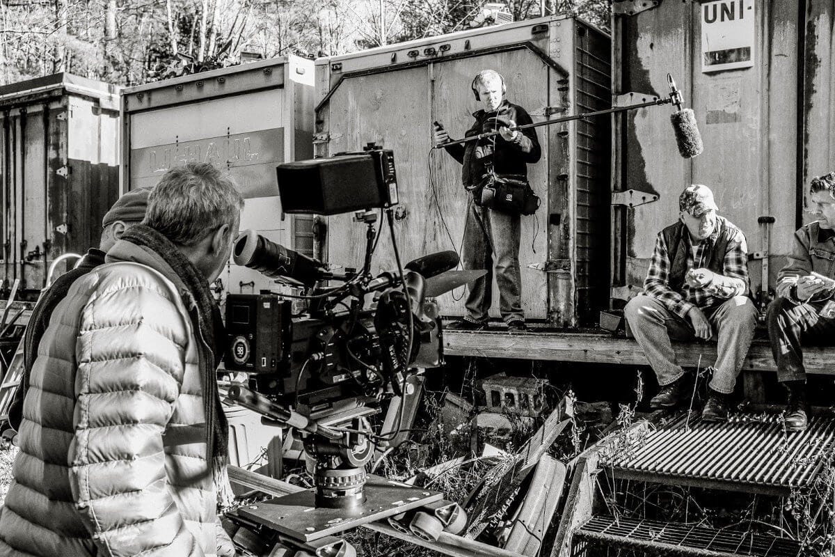 A black-and-white shot of Aaron Weisblatt filming a movie outside near some shipping containers