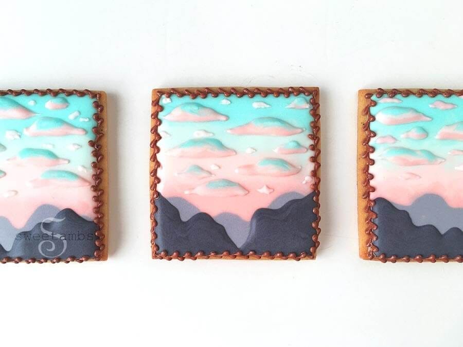 Decorated cookies showing a mountainside beneath colorful clouds by cookie artist Amber Spiegel (SweetAmbs)