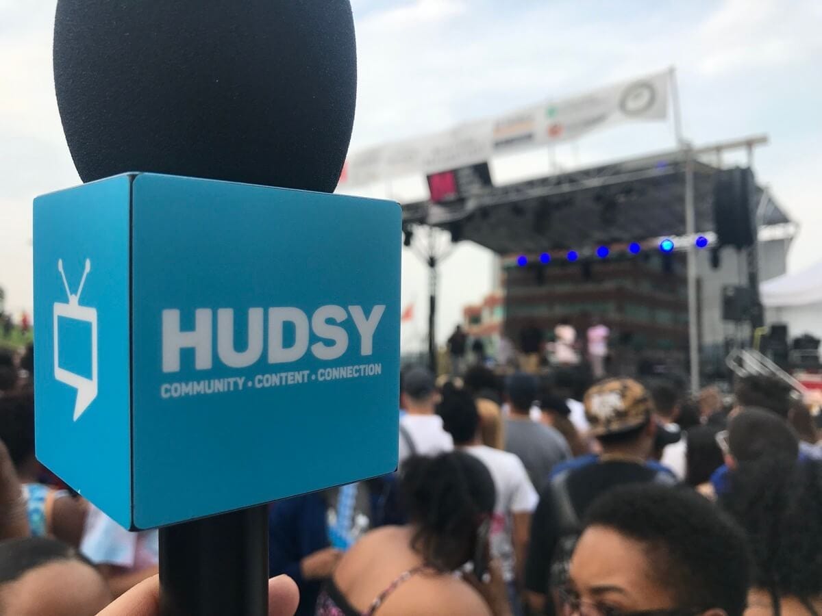 A HUDSY logo on a microphone in front of a stage at a Hudson Valley event