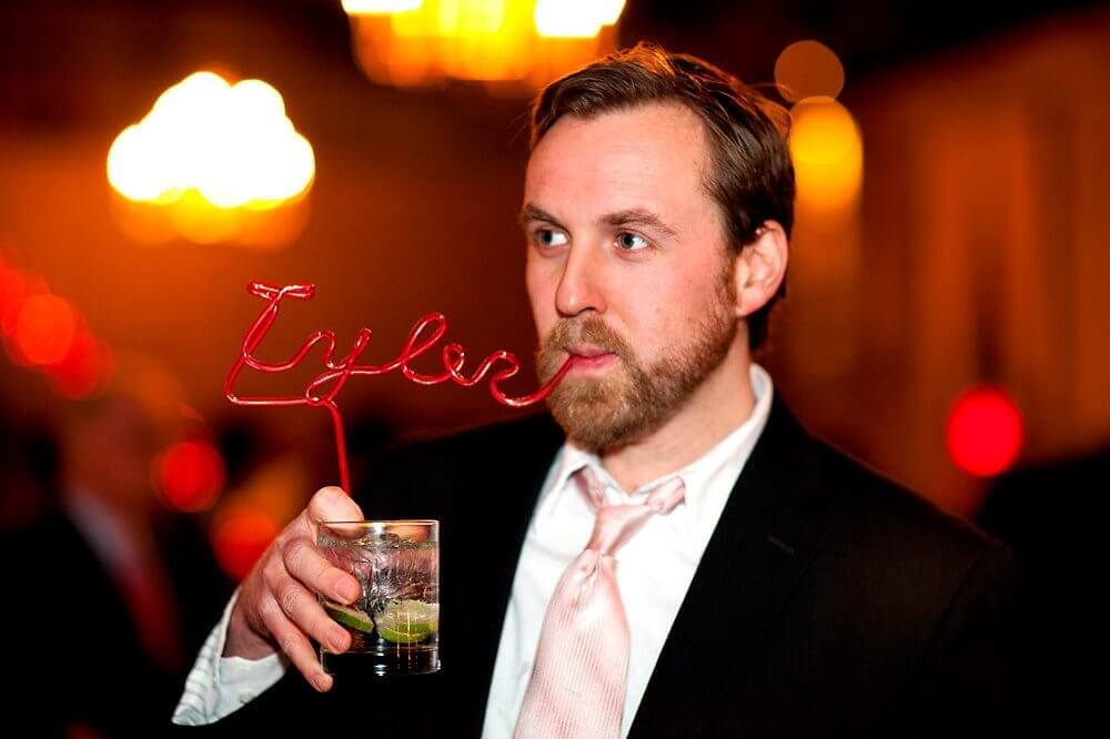 Tyler Walker wearing a suit drinking through a straw that spells "Tyler"